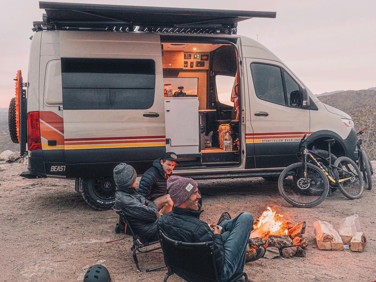 two men sit outside their campervan with a fire to keep warm